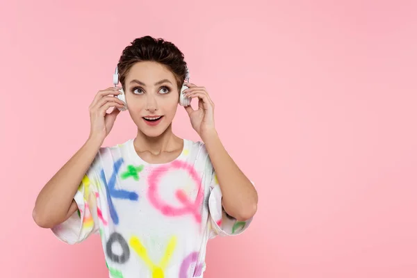 Alegre Morena Mujer Ajustando Auriculares Mientras Escucha Música Aislada Rosa — Foto de Stock