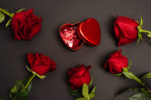 horní pohled na kovovou krabici s červenými konfety srdce v blízkosti růží na černé