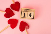 plochá poloha lízátek ve tvaru srdce poblíž dřevěného kalendáře se 14 únorovými na růžové 