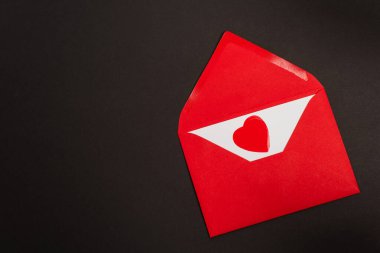 Aşk mektubu ve kağıt içeren kırmızı zarfın üst görüntüsü siyah üzerine izole edilmiş kalbi kesiyor. 