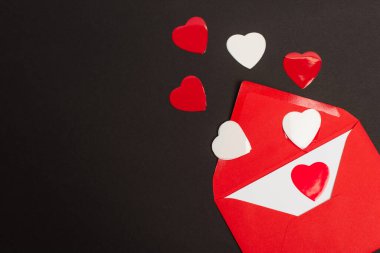 Üzerinde aşk mektubu ve kağıt olan kırmızı zarfın üst görüntüsü siyah kalplere izole edilmiş. 