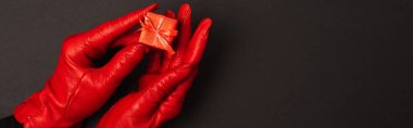 cropped view of woman in red gloves holding tiny gift box on black, banner clipart
