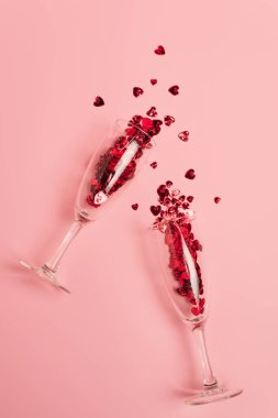 Şampanya bardaklarının üst görüntüsü, pembe üzerinde kırmızı konfeti kalpleri olan.