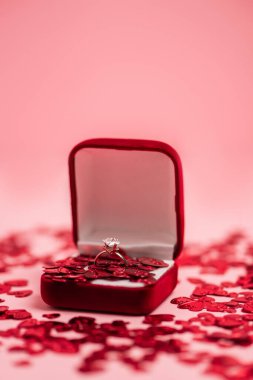 close up of jewelry box with diamond ring near shiny confetti hearts on pink clipart