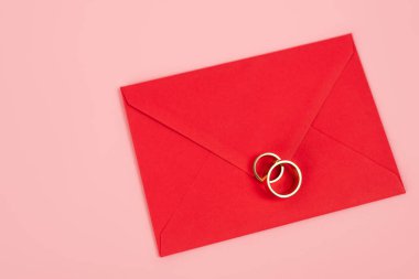 Kırmızı zarf üzerindeki yüzüklerin üst görüntüsü pembe üzerine izole edilmiş 