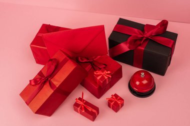 Kırmızı paketlenmiş hediye kutularının yüksek açılı görüntüsü ve pembe üzerindeki metalik çanın yanındaki zarf 