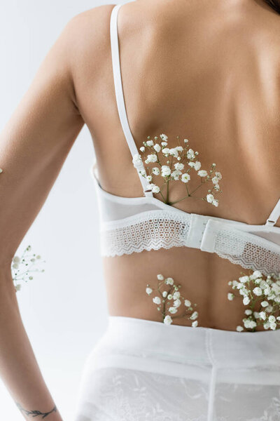 partial view of young woman in lace bra, with white flowers on body isolated on grey
