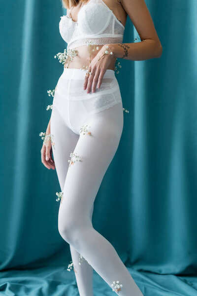 partial view of slim woman in lace bra and tights with white tiny flowers standing on green draped background