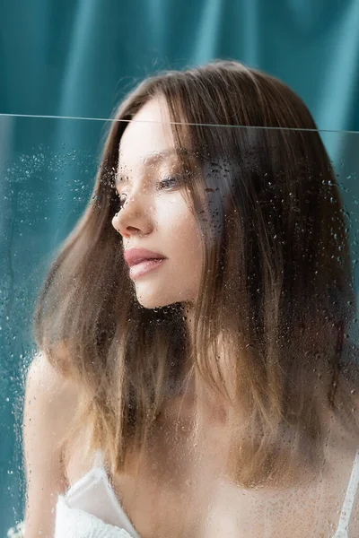 濡れたガラスの近くに官能的なブルネットの女性と背景にターコイズドレープ — ストック写真