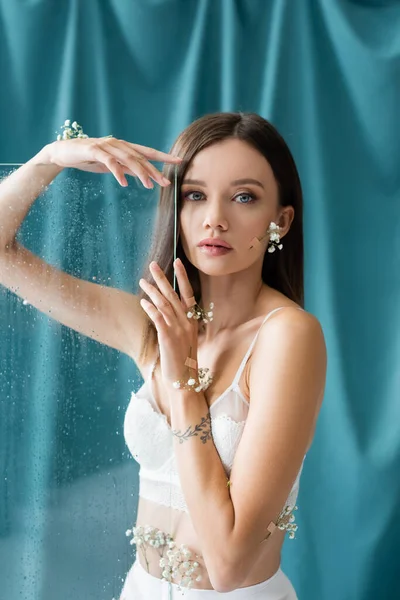 Sütyeninde ıslak cam ve arka planda yeşil perde olan küçük çiçeklerle süslenmiş baştan çıkarıcı bir kadın.