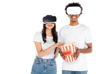 Beyaz tenli patlamış mısırın üzerinde vr kulaklıklarla oynayan mutlu ırklar arası çiftler.