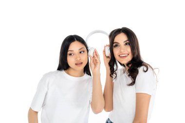 Mutlu ırklar arası kadınlar ellerinde kulaklıklarla beyazlara izole edilmiş müzik dinliyorlar.