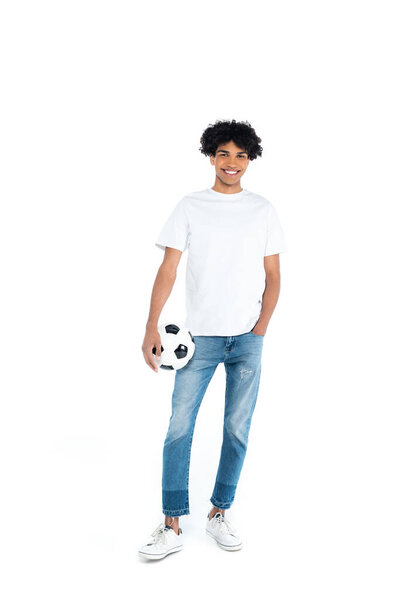 happy african american man standing with hand in pocket while holding soccer ball on white