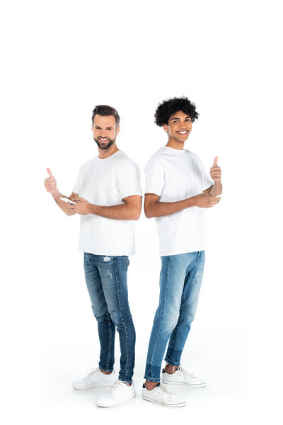 full length view of smiling multiethnic men with smartphones showing thumbs up on white