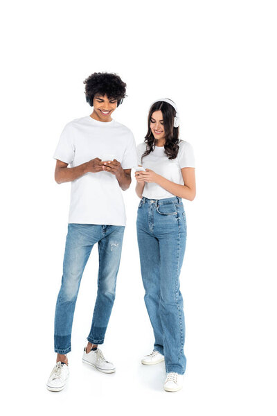 interracial couple in jeans and headphones using mobile phones on white