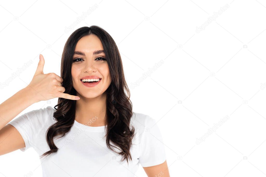 excited brunette woman showing call me gesture while looking at camera isolated on white