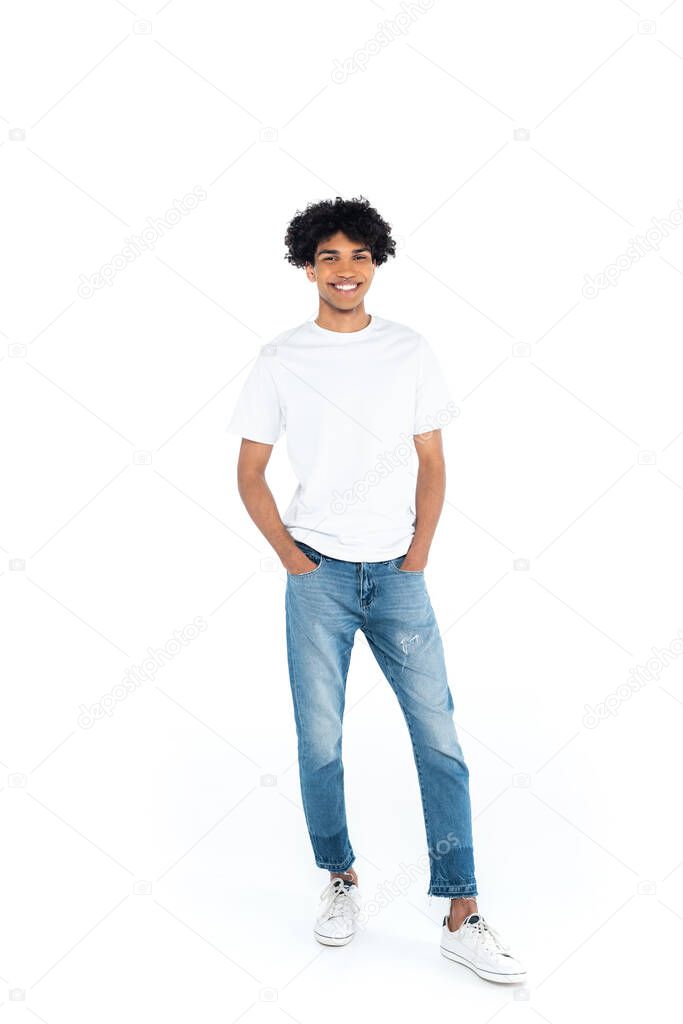 full length view of smiling african american man standing with hands in pockets of jeans on white