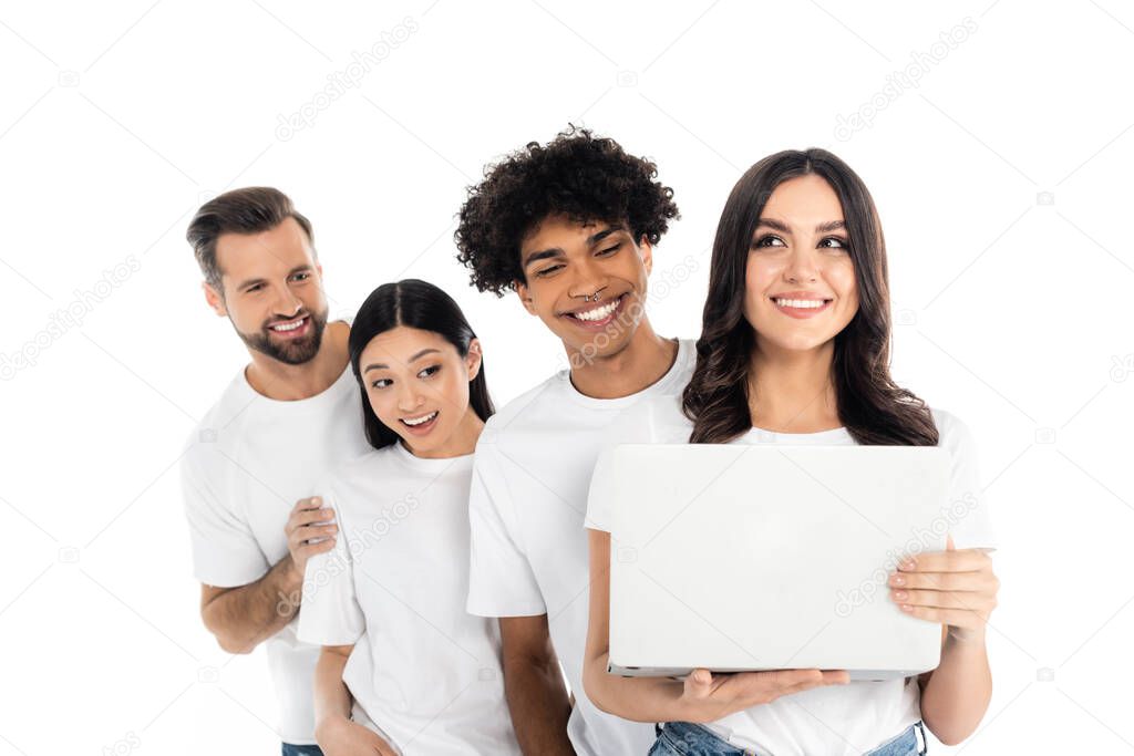 young cheerful woman holding laptop near cheerful interracial friends isolated on white