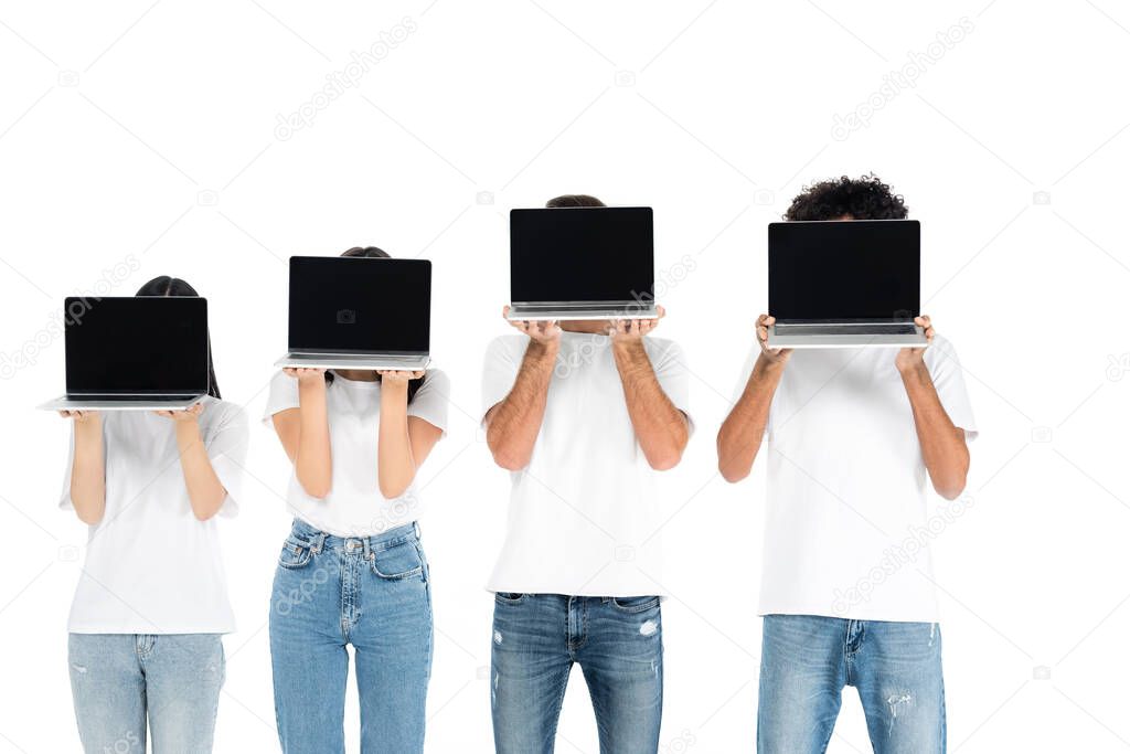 multiethnic friends in t-shirts and jeans obscuring faces with laptops with blank screen isolated on white