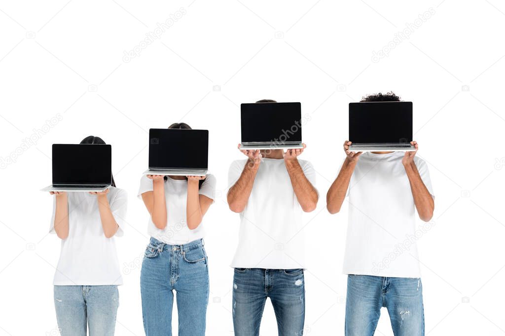 multicultural friends in jeans and t-shirts obscuring faces with laptops with blank screen isolated on white