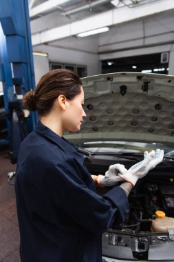 Servis sırasında otomobilin yanında eldiven takan genç tamircinin yan görüntüsü 