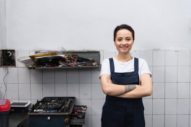 Garajdaki aletlerin yanında dövmeli bir tamirci kollarını kavuşturuyor. 