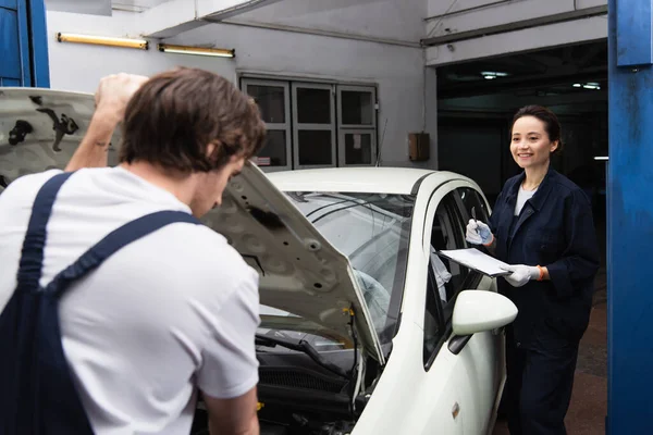 Positive Workwoman Holding Clipboard Blurred Colleague Car Service — Fotografia de Stock