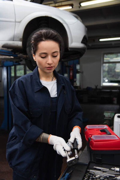 Workwoman in gloves taking tool near toolbox in car service 