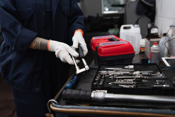 Cropped view of handywoman holding tool near wrenches in car service
