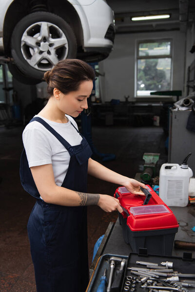 Mechanic in overalls opening toolbox near blurred car in service 