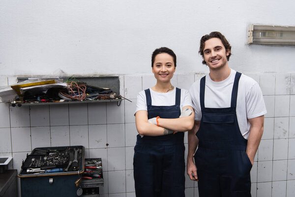 Smiling mechanics looking at camera near tools in car service 