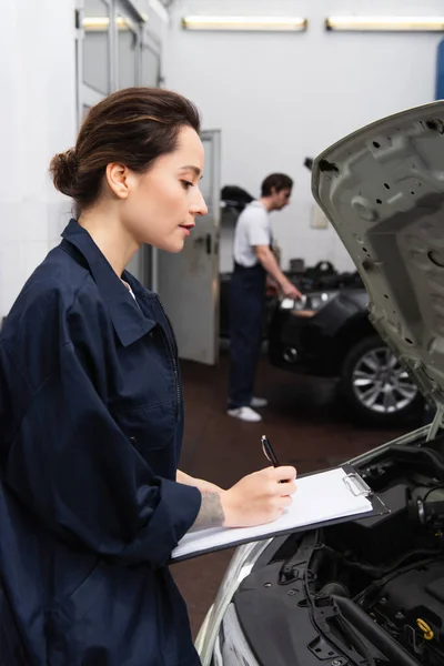 Side View Mechanic Writing Clipboard Car Open Hood — Stock Photo, Image