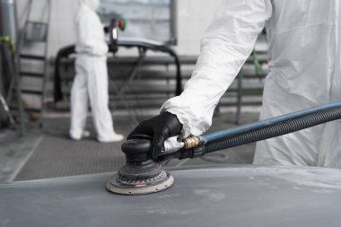 Cropped view of workman in hazmat suit polishing car in garage  clipart