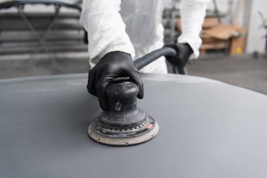 Cropped view of workman in gloves and hazmat suit polishing car in garage  clipart