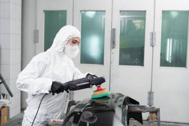 Workwoman in protective suit polishing car part in service  clipart