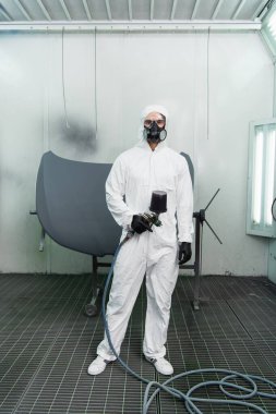 Koruyucu takım elbiseli ve gözlüklü işçi araç servisinde aerograf tutuyor. 