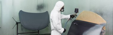 Workman in respirator and hazmat suit coloring car part in service, banner  clipart