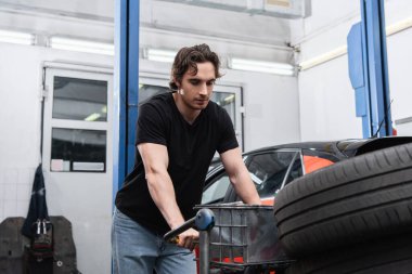 Mechanic standing near cart with tire in service  clipart