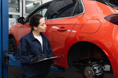 Otomobil servisindeki arabanın yanındaki panoya üniformalı bir işçi yazıyor. 