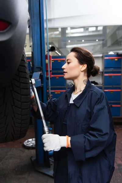 Ustabaşı Üniformalı Kadının Garajda Araba Tekerleğinin Yanında Ingiliz Anahtarı Tutarken — Stok fotoğraf