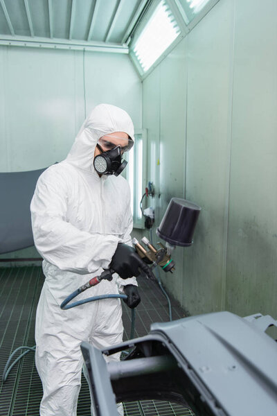 Workman holding aerograph near blurred car part in garage 