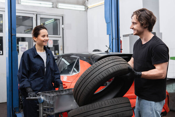 Smiling mechanics standing near tires and blurred car in garage 