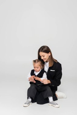 happy mother touching hand of child with down syndrome isolated on grey