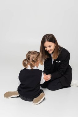 cheerful mother touching hands of child with down syndrome isolated on grey