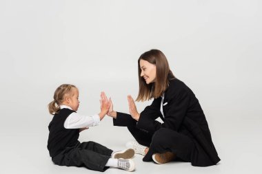 side view of cheerful mother playing patty cake with disabled girl on grey