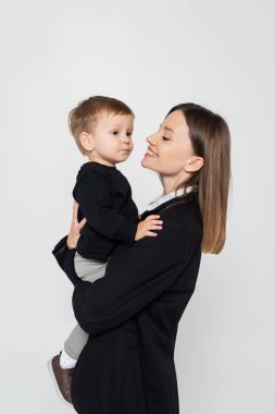 happy mother holding in arms toddler son isolated on grey
