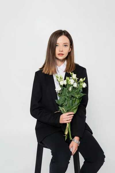 Молода Стильна Жінка Костюмі Тримає Букет Квітів Сидить Стільці Ізольовано — стокове фото