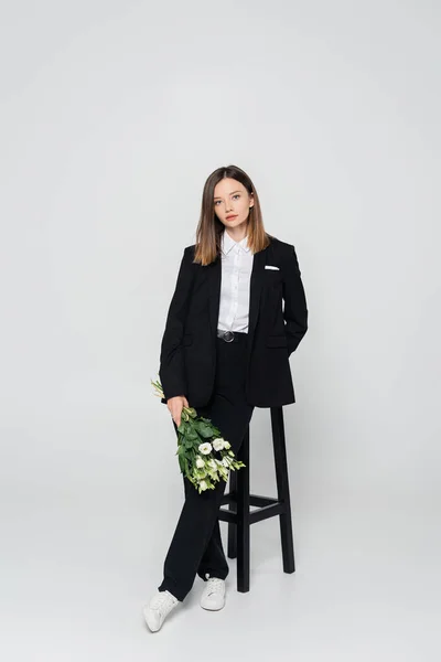 Full Length Young Woman Suit Holding Bouquet Flowers Leaning Chair — Zdjęcie stockowe