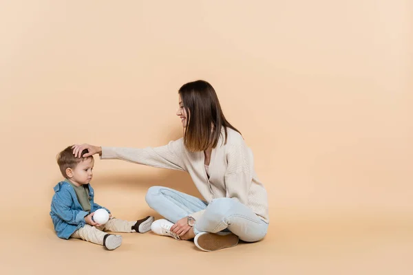 Happy Mother Sitting Adjusting Hair Toddler Son Beige — Stok fotoğraf