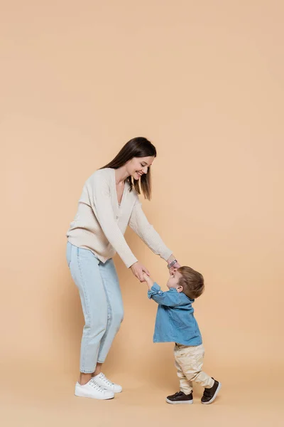 Full Length Cheerful Mother Standing Holding Hands Toddler Son Beige — Stock Photo, Image